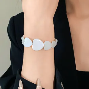 Close-up view of a minimalist white heart-shaped shell bracelet worn on a wrist.