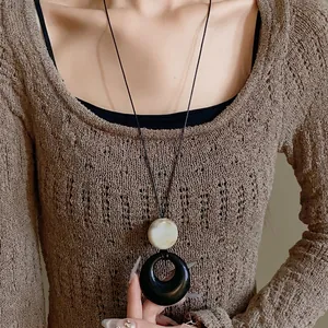 Minimalist resin ring long necklace with black and marble pendant on brown sweater.
