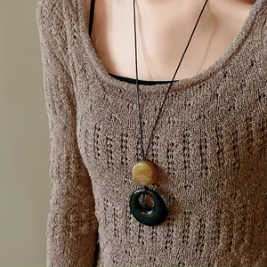 Close-up of a retro geometric resin ring pendant worn with a brown knitted sweater.
