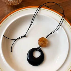 Close-up detail of a minimalist resin ring necklace with amber bead on a white plate