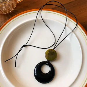 Close-up of a minimalist resin ring necklace with olive green bead and black cord.