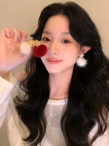 Close-up of model wearing fluffy white and red pom-pom earrings with gold accents