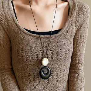 Macro detail of a black resin ring pendant necklace worn over a cozy brown knitted sweater.