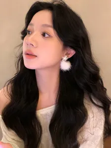 Close-up of elegant snowflake earrings with white fluffy fur balls worn by model