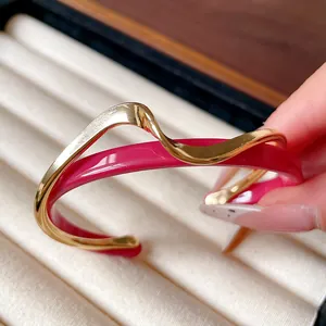 Detalle del brazalete rígido de doble capa ondulada chapada en oro y rosa fucsia.