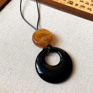 Close-up detail of a minimalist resin ring necklace with amber bead on a black cord.