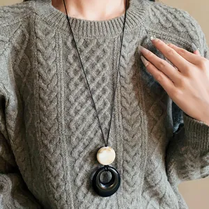 Close-up of the geometric resin ring necklace worn on a gray knitted sweater.