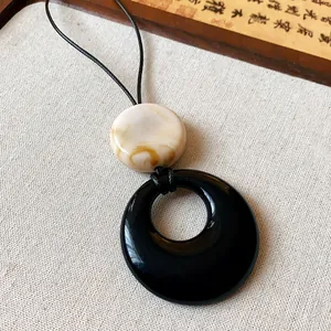 Detailed close-up of a minimalist resin ring necklace with black and marbled beige discs