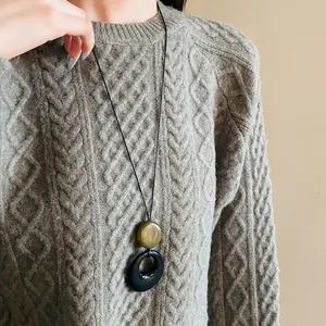 Close-up of a stylish resin ring pendant necklace worn over a grey cable-knit sweater.
