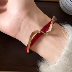 Primer plano de un brazalete abierto de acrílico dorado ondulado en una muñeca con jersey