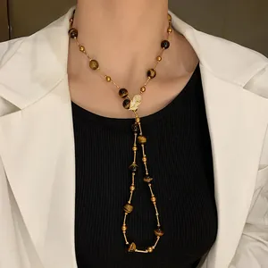Detail of a vintage long necklace with tiger eye beads and leaf pendant worn by model