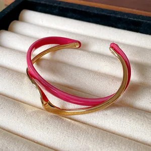 Detalle de un brazalete abierto de doble capa ondulada bañada en oro con acrílico rosa.
