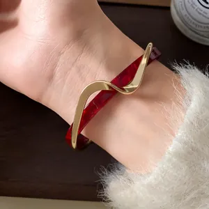 Detalle de cerca del brazalete de onda en acrílico rojo y chapado en oro en la muñeca
