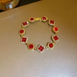 Elegant gold bracelet with red crystals and diamond-encrusted four-leaf clover charms.