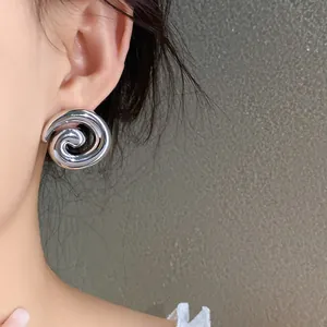 Macro view showing a shiny silver spiral geometric stud earring worn on a model's ear