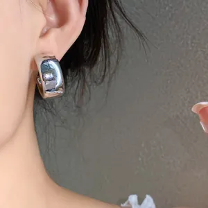 Detailed close-up view of a glossy silver geometric hoop earring worn on a model's ear