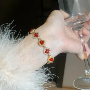 Detailed view of an elegant gold bracelet featuring red floral stones worn on a wrist holding a glass