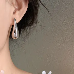 Silver polished teardrop stud earrings worn on ear showing an elegant minimalist style