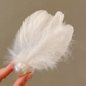 Detail shot of an elegant white feather hair clip with a large central pearl embellishment.