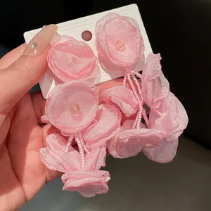 Close-up of handmade pink fabric flower stud earrings with delicate glass bead tassels
