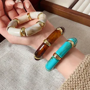 Stacked bohemian cylindrical elastic bracelets featuring marbled resin and gold-tone spacers.