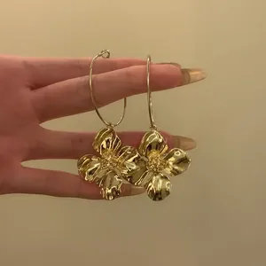 Detailansicht goldener Creolen mit strukturierten Blumenanhängern, handgehalten