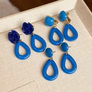Gros plan de boucles d'oreilles fleurs en acrylique bleu sur un plateau beige.