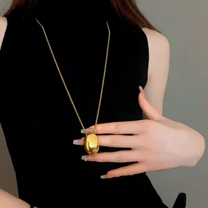 Close-up detail of a minimalist gold oval pendant necklace worn on a black top