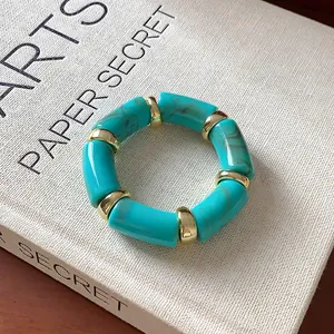 Detail view of a turquoise marbled cylinder bead bracelet with gold spacers on a book.