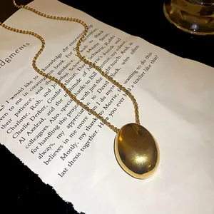 Polished gold oval pendant necklace made of stainless steel on a vintage book page backdrop