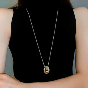 Close-up detail of a polished silver stainless steel oval pendant necklace on a long chain