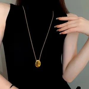 Close-up of a minimalist gold oval pendant necklace worn on a black turtleneck.
