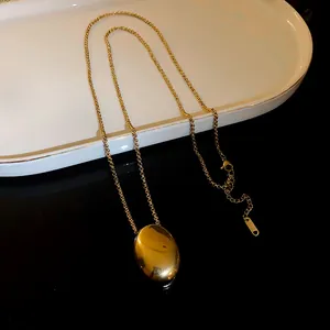 Detailed view of a gold titanium steel necklace with an oval pendant on a white tray