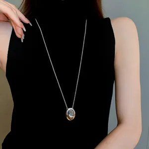 Detail view of a sleek titanium steel oval pendant necklace worn over a black turtleneck.