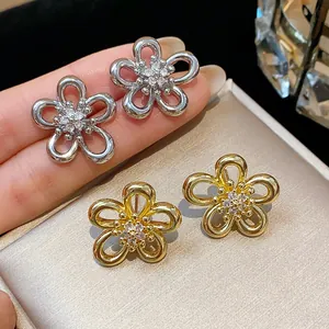 Detailed close-up of silver and gold flower stud earrings with sparkling zircon centers.