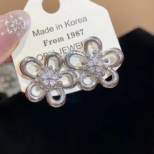 Close-up detail of silver flower stud earrings with a central sparkling zircon cluster.
