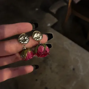 Detailed view of French vintage preserved red rose bud drop earrings held by hand