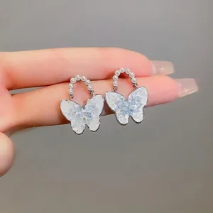 Elegante Schmetterling-Ohrstecker mit Kristall-Inlay und Perlen-Detail auf grauem Grund