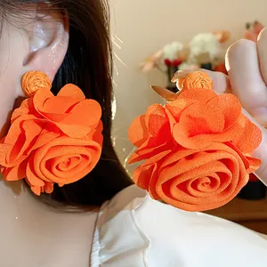 Close-up detail of oversized orange chiffon rose earrings with raffia base