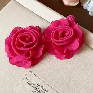 Macro view of elegant red chiffon rose flower earrings placed on a textured gift box