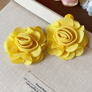 Close-up detail of elegant yellow chiffon flower earrings on a textured beige display