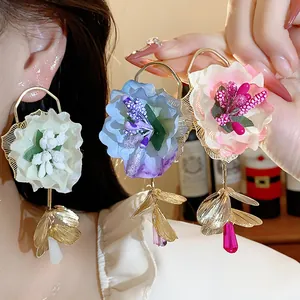 Close-up of elegant fabric floral earrings with glass accents and gold leaf details.
