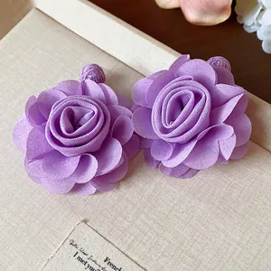 Close-up of elegant purple chiffon flower earrings with raffia accents on a textured surface.
