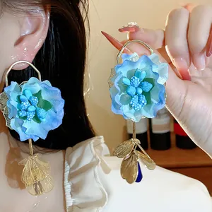 Macro detail shot of blue fabric flower earrings featuring elegant golden petal pendants