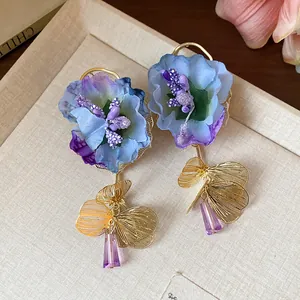 Close-up of elegant fabric flower earrings featuring purple glass drop and gold petals.