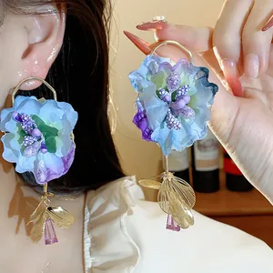 Detail of exaggerated blue fabric flower earrings with gold leaf and purple crystal drops.
