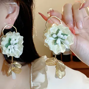 Detailed close-up of oversized fabric floral earrings featuring gold-tone leaf charms.