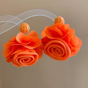Detailed macro view of bright orange chiffon rose earrings with raffia accents