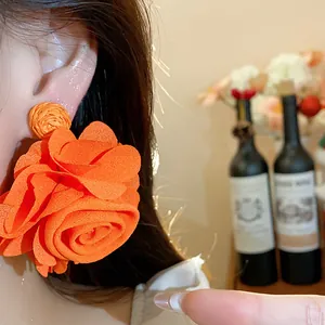 Close-up of bright orange chiffon flower earring with handwoven raffia detail on model's ear