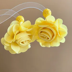 Macro detail of elegant yellow chiffon flower earrings with raffia woven ball studs.